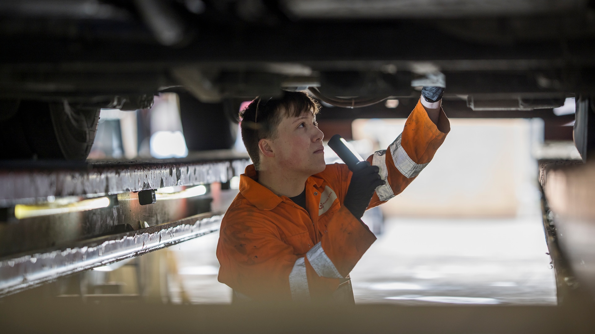 a man in an orange jumpsuit holding a flashlight up under a car